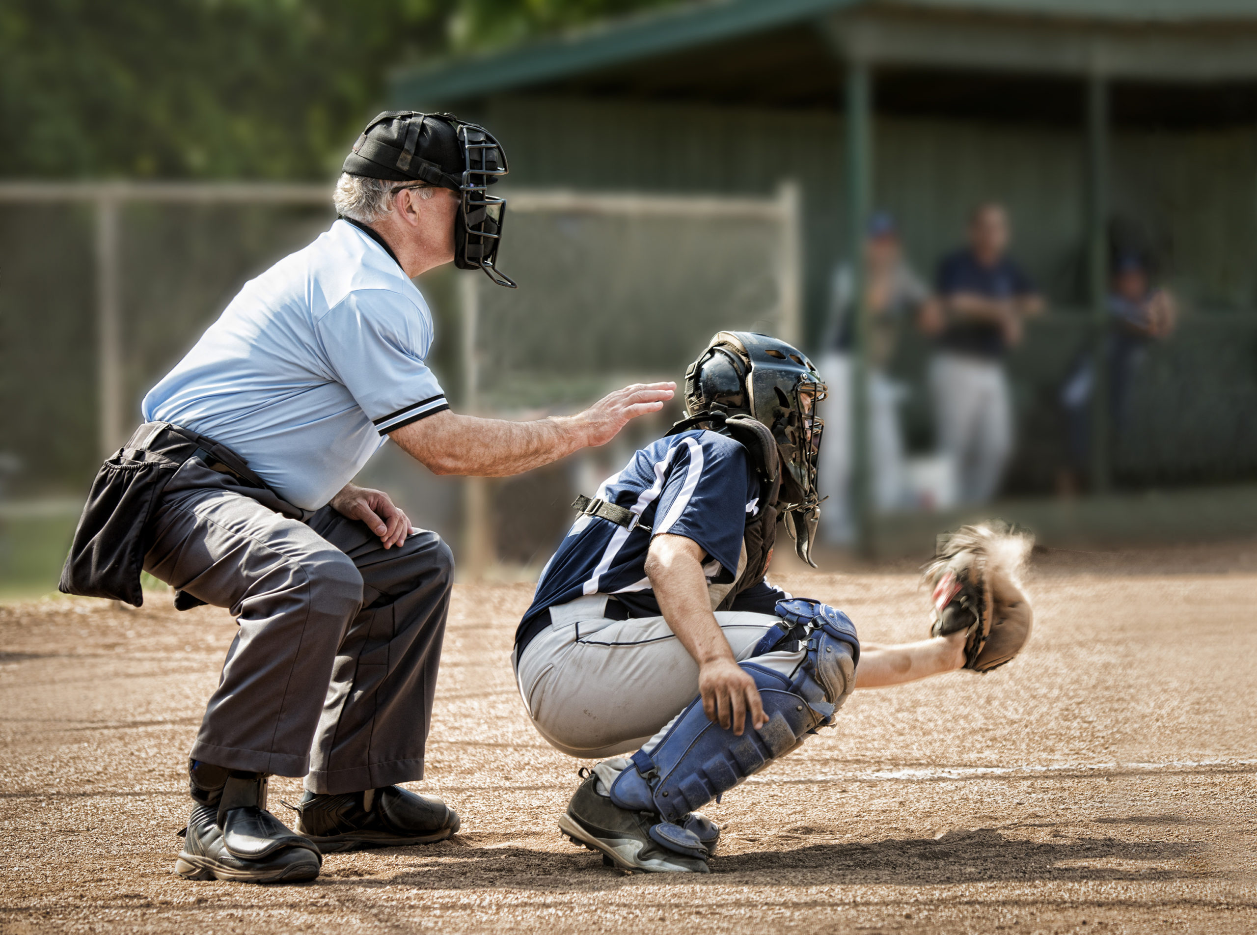 Umpire and catcher, just as ball hits catcher's mitt, dugout and players in background