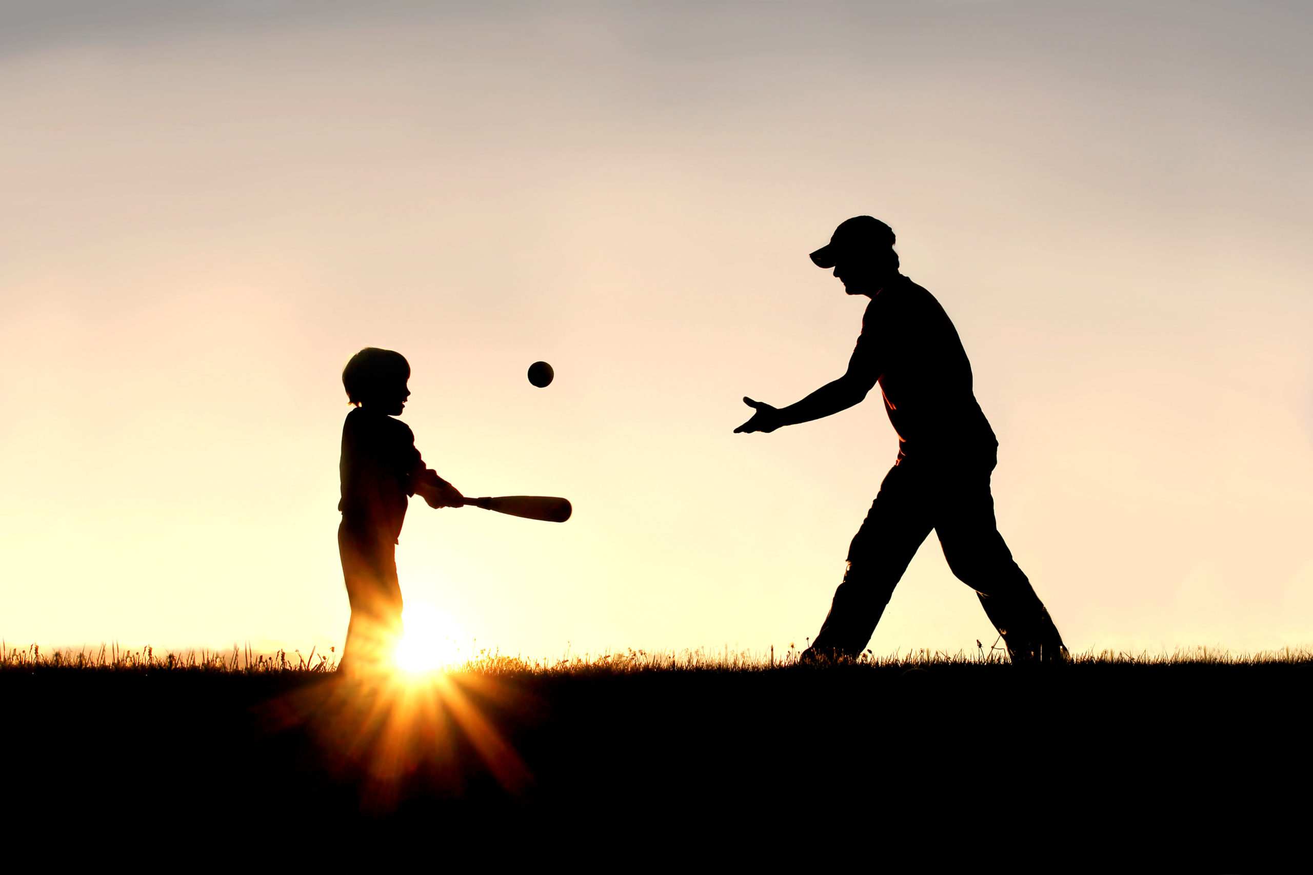 Silhouette of Father and Son Playing Baseball Outside Coach pitching ball to player at dusk